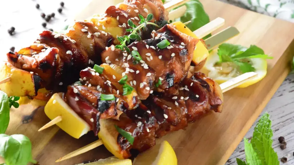 Aromatyczne yakitori z kurczaka w sosie teriyaki, posypane sezamem, z kawałkami ananasa i cytryny na drewnianej desce.