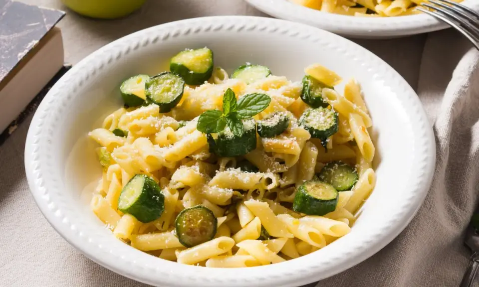 Pyszne danie z makaronem penne i kawałkami cukinii, posypane parmezanem i listkami mięty. Idealne co z cukinii na obiad!