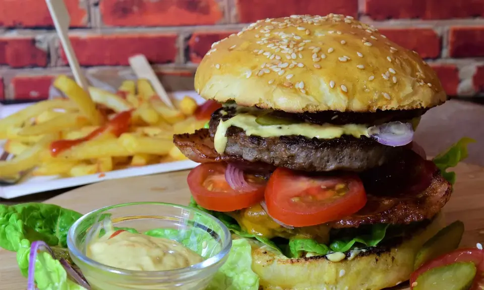 Soczysty burger z wołowiny, bekonem, warzywami i frytkami w tle.