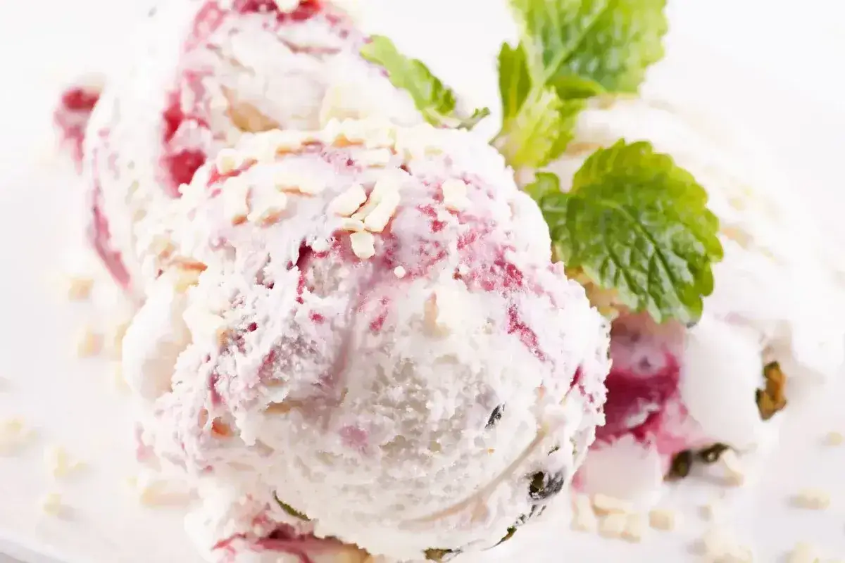 Pyszne lody z mascarpone z malinową nutą i chrupiącymi kawałkami białej czekolady, ozdobione listkiem mięty.