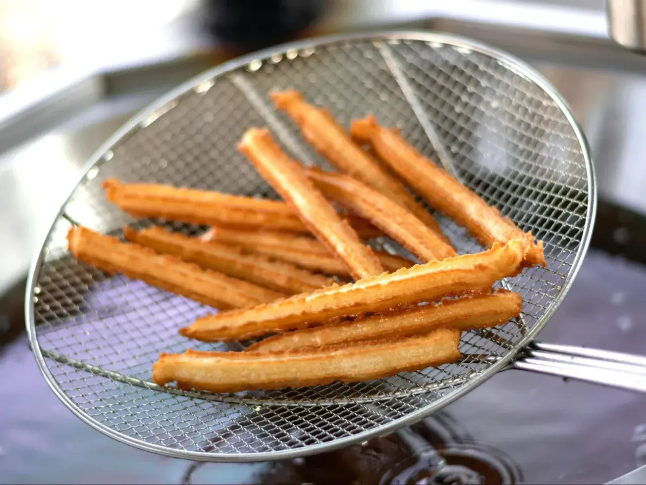 Churros co to? Złociste, chrupiące paluszki smażone na głębokim tłuszczu, wyjęte właśnie z frytownicy na metalowej łyżce cedzakowej.