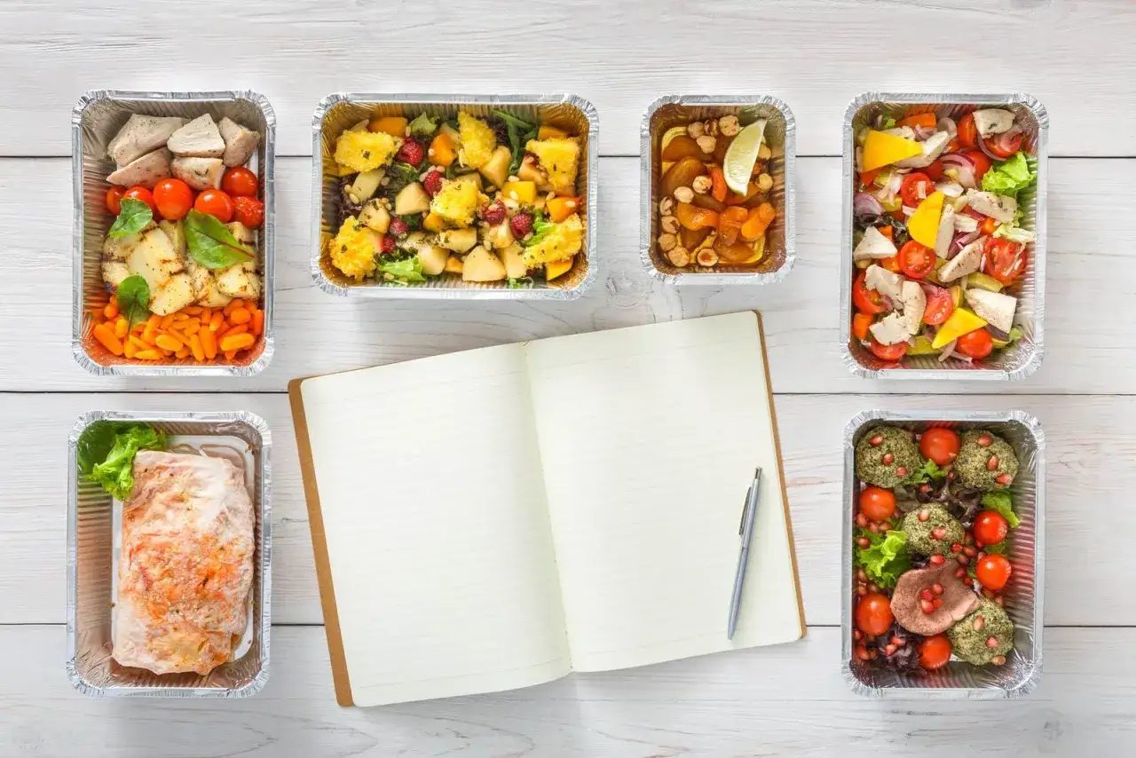 Planujesz catering dietetyczny? Warto sprawdzić, jak wyglądają zdrowe posiłki w pudełkach, obok otwartego notatnika.
