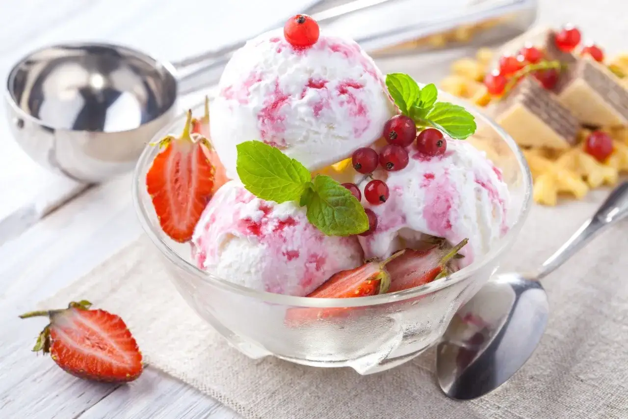Pyszne lody z mascarpone, udekorowane truskawkami i porzeczkami, kuszą swoim kremowym smakiem.