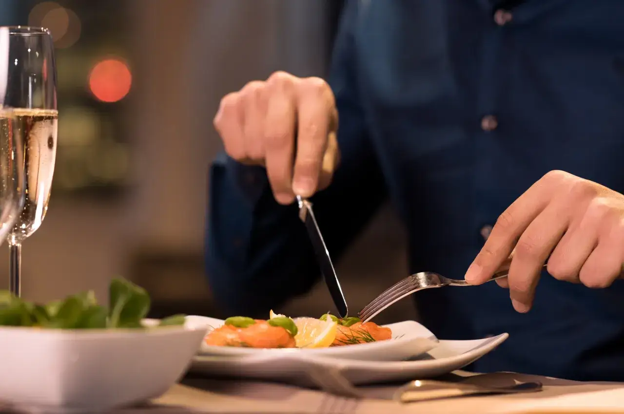 Mężczyzna kroi łososia, delektując się wykwintnym daniem. Tak jesc catering to prawdziwa przyjemność.