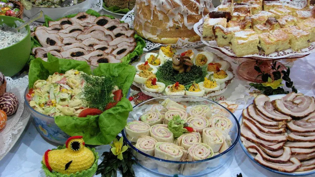 Wielkanocny stół pełen pyszności: pieczone mięsa, sałatki, jajka faszerowane, babka i ciasta. Idealne inspiracje, co ugotować na Święta Wielkanocne.
