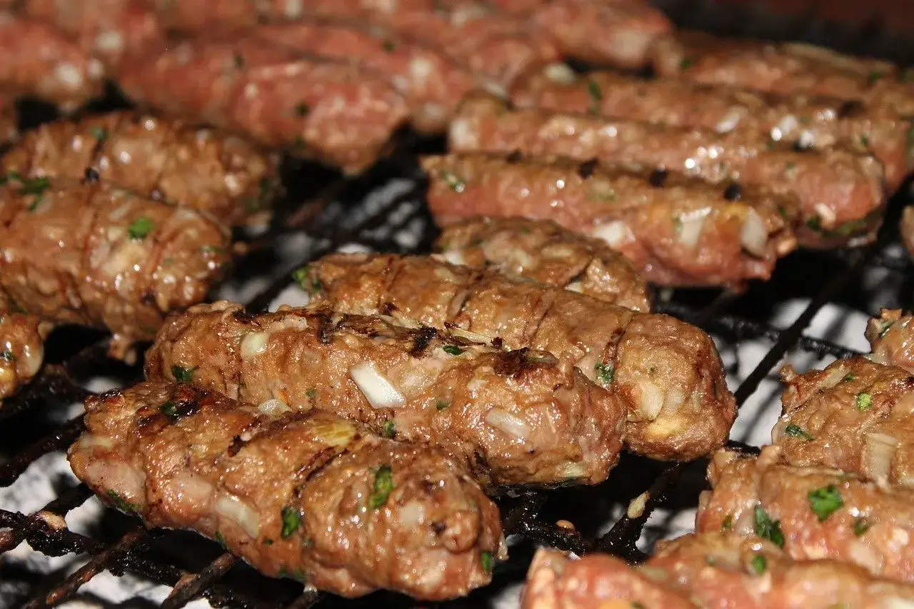 Soczyste cevapi piekące się na grillu, z widocznymi kawałkami cebuli i ziół.
