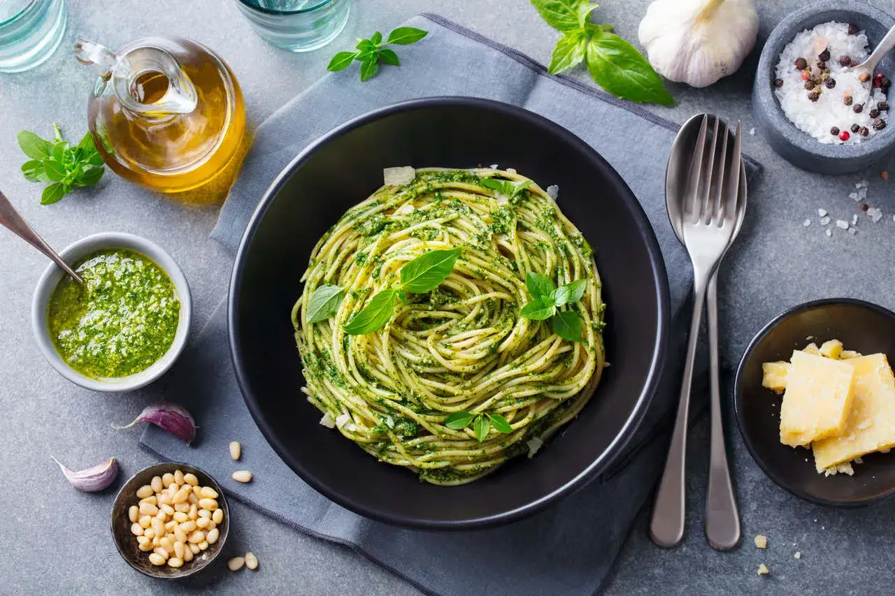 Pyszne spaghetti z pesto, idealne jako co na obiad dla gości. Podane z parmezanem, orzeszkami pinii i świeżą bazylią.