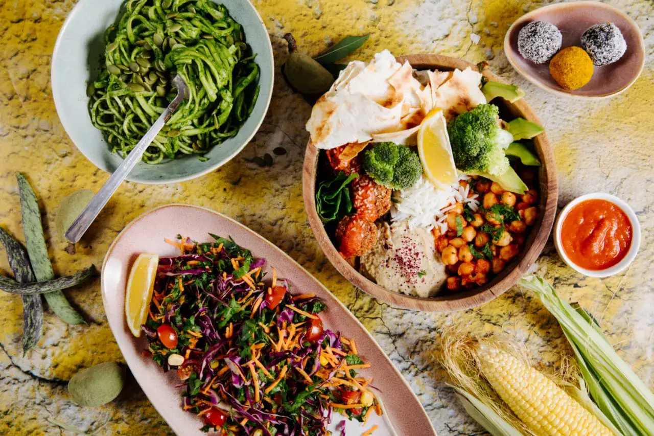 Kolorowe dania wegetariańskie: makaron z pesto, miska z hummusem, falafelami i warzywami, sałatka z czerwoną kapustą. Idealne co na obiad wegetariański.