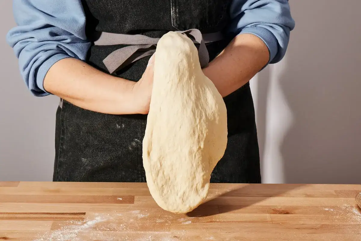 Osoba w fartuchu ugniata ciasto na pizzę. To kluczowy etap w przygotowaniu najlepsza pizza przepis.