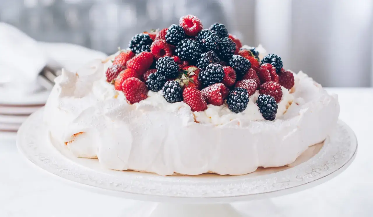 Beza pavlova która zawsze wychodzi, udekorowana bitą śmietaną i obficie posypana świeżymi malinami, jeżynami i truskawkami.