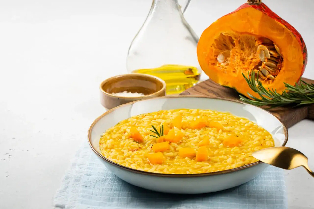Pyszne risotto z dyni, idealne na jesienny obiad. Obok miski leży przekrojona dynia, gałązka rozmarynu i oliwa.