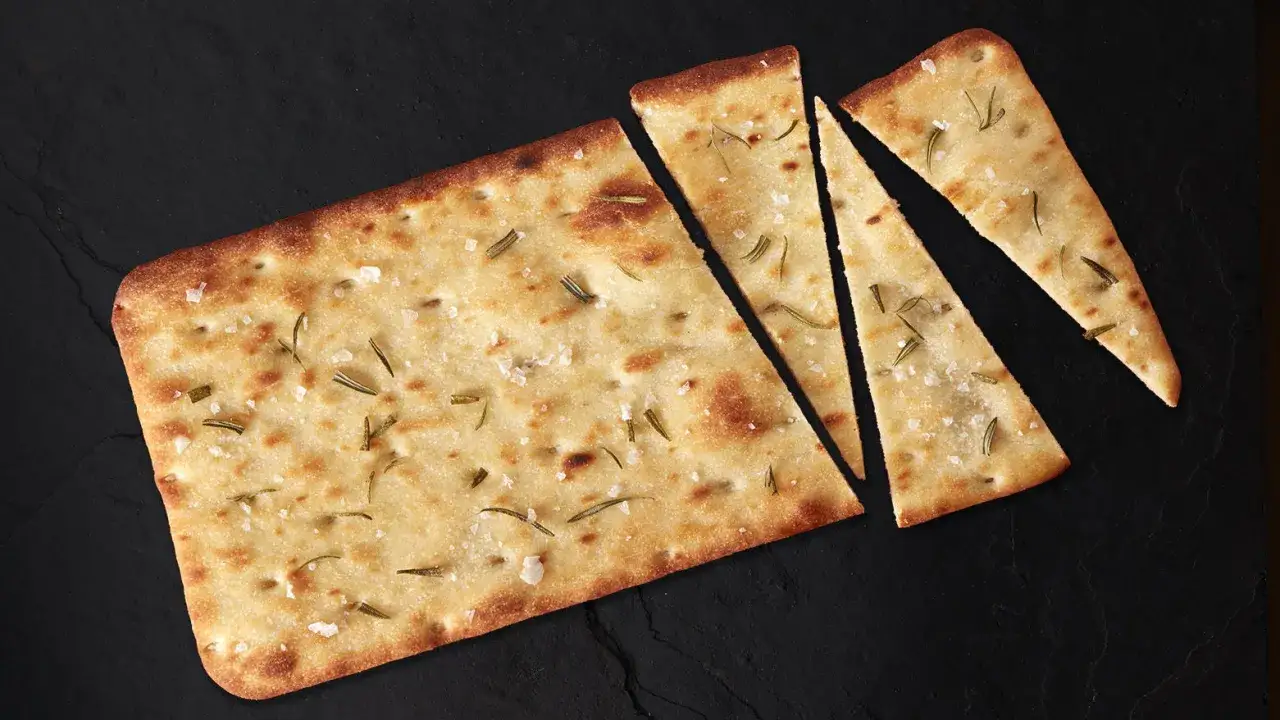 Chrupiąca pizza bianca z rozmarynem i solą morską, pokrojona na kawałki, wygląda apetycznie.