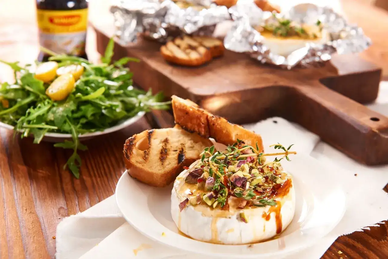 Pyszny camembert z grilla, polany miodem i posypany pistacjami, podany z grzankami i sałatką.