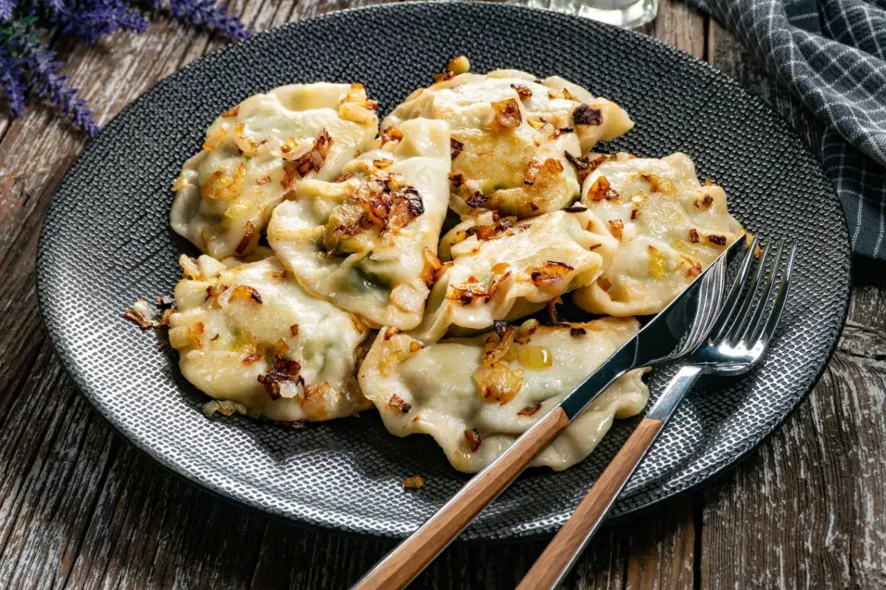 Pyszne pierogi z cebulką, idealne, gdy zastanawiasz się, czy można gotować mrożone pierogi. Podane na talerzu z widelcem i nożem.