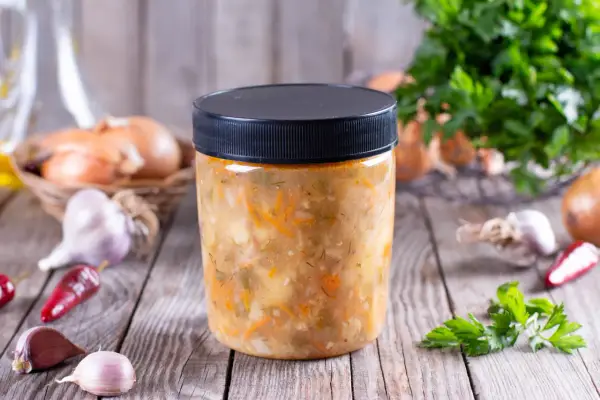 Słoik z domową zupą warzywną, obok cebula, czosnek i chili. Dowiedz się, jakich zup nie można mrozić.