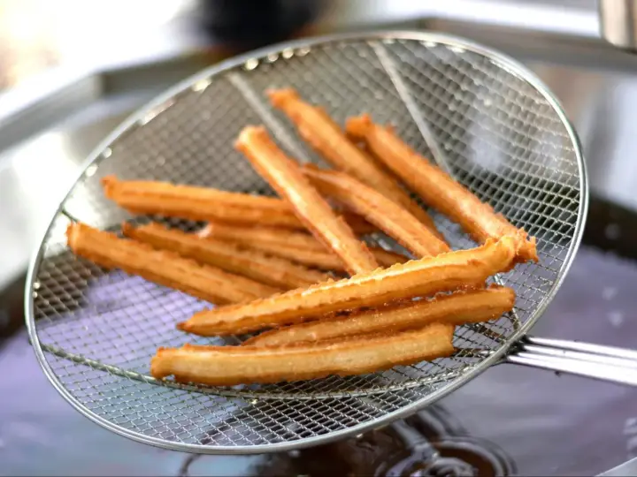 Churros co to? Złociste, chrupiące paluszki smażone na głębokim tłuszczu, wyjęte właśnie z frytownicy na metalowej łyżce cedzakowej.