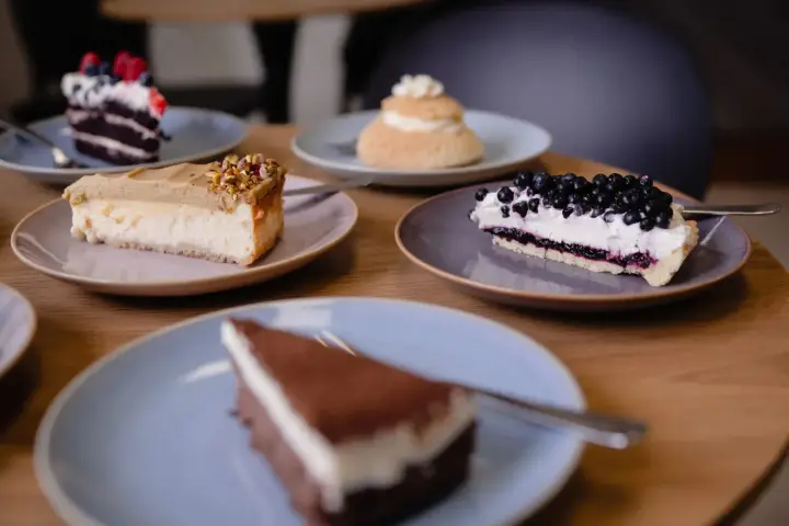 Kawa, jagody, pistacje – te składniki to klucz do najmodniejszych ciast. Na stole pięć pysznych deserów, każdy na osobnym talerzyku.